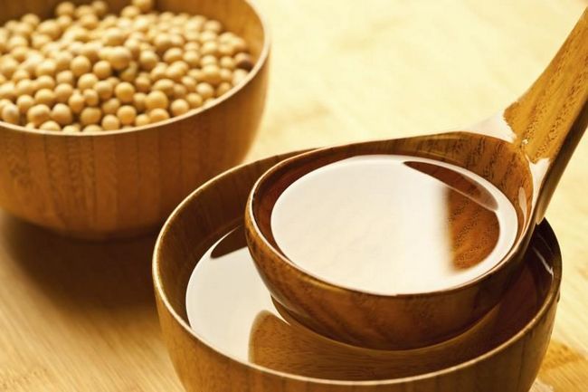 Une petite cuillère d'huile de soja, à côté d'un bol de graines de soja.