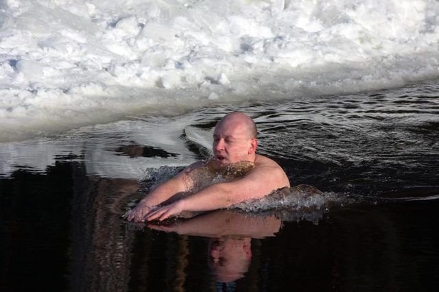 Un homme nageant dans l'eau à côté de la glace et de la neige.