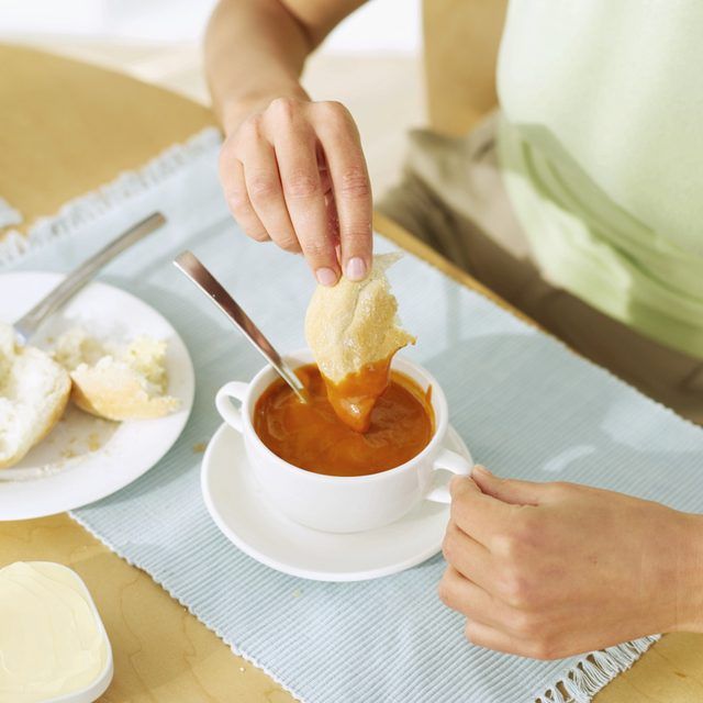 Une personne est tremper le pain dans la soupe de tomate.