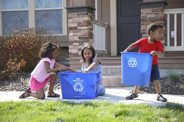 Trois jeunes enfants organisant des bacs de recyclage.