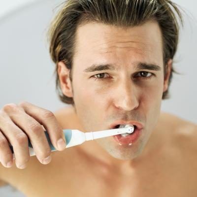 Portrait d'un jeune homme se brosser les dents avec une brosse à dents électrique.