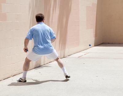 Un homme prend une position large squatté tout en jouant au racquetball extérieur.