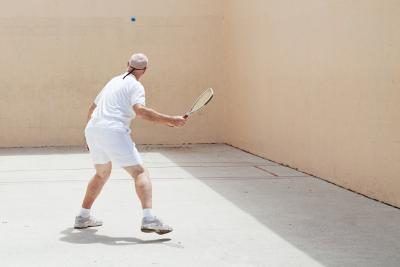 Un haut frappe une balle au mur sur un terrain de racquetball extérieure.
