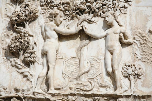 Un gros plan d'une sculpture en relief d'Adam et Eve tenant le serpent dans le jardin.