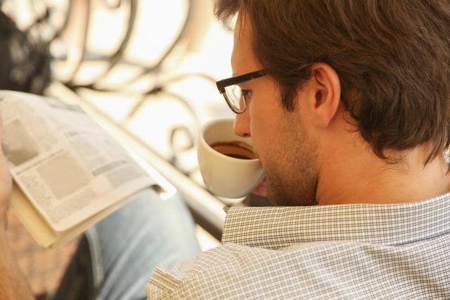 Un homme lisant en savourant du café à une table ensoleillée.