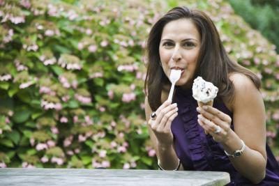 Une femme mange un cornet de glace sur un banc.