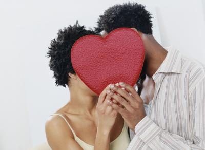 Un homme et une femme sont embrassés derrière un coeur rouge.
