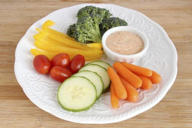 Tranches de concombre, carotte, poivrons jaunes, et le brocoli dans une assiette avec des tomates cerises et un côté du dressing.
