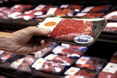 Une femme regarde un paquet de viande de bœuf dans le supermarché.