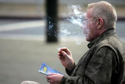 Homme fume cigarette sur un banc de parc.