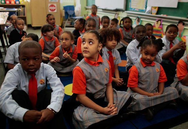 Les élèves du primaire portant des uniformes scolaires sont assis sur un tapis dans la salle de classe.
