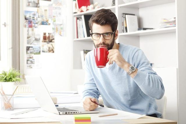 Un homme sirote un café dans son bureau de bureau avec des étagères en arrière-plan.